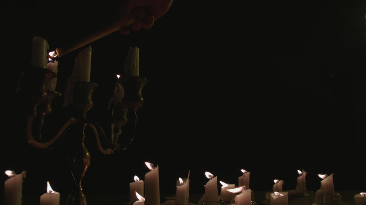 Un gruppo di candele bianche, alcune su un candelabro, che si accendono e bruciano per un po'