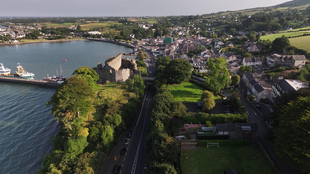 Carlingford town drone pull back, reveal castle in evening golden light. Ireland