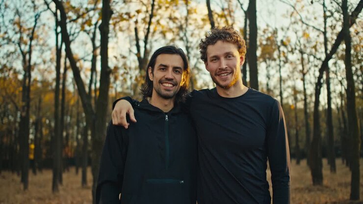 Portrait of two happy guys with black hair and beard in black sportswear who are on a morning jog in the autumn forest in the morning. Two guys are hugging and posing in the morning In the forest