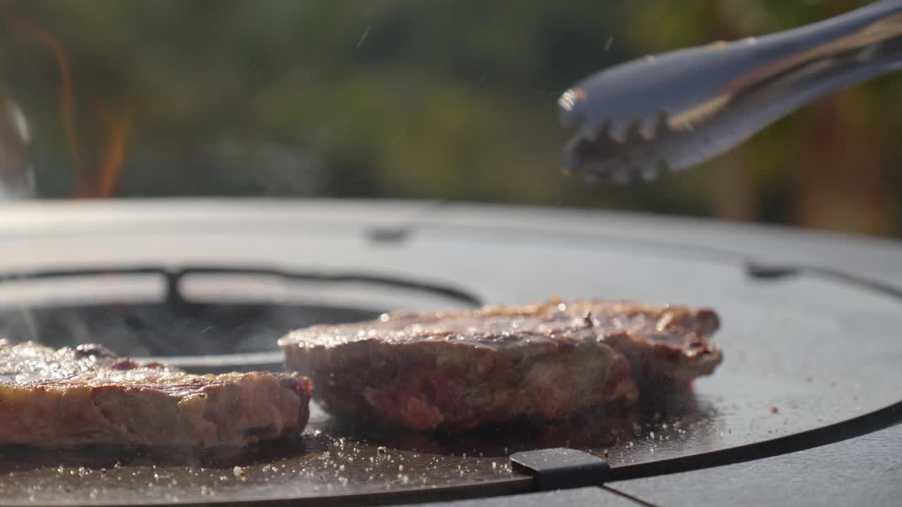 slowmotion of a sirloin steak being flipped to brown both sides on a BBQ