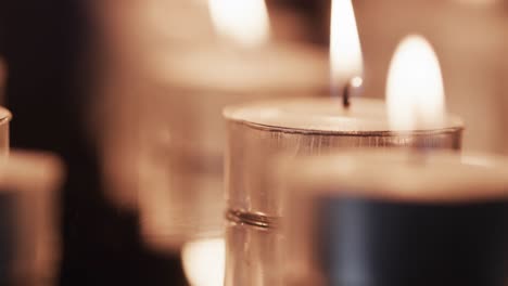 Video-of-close-up-of-rows-of-tea-candles-with-white-flames-and-copy-space-on-black-background