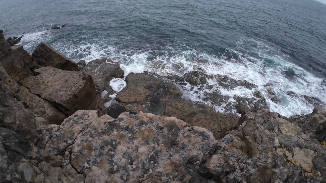 Un video girato con drone cattura una straordinaria vista aerea delle onde che si infrangono sulle rocce rustiche a Dancing Ledge, Isle of Purbeck. L'illuminazione drammatica e le formazioni aspre creano una scena costiera dinamica.