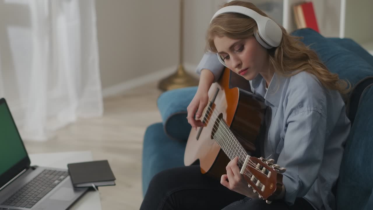 sad woman is playing acoustic guitar sitting in front of notebook with green screen, online concert or streaming of home gig