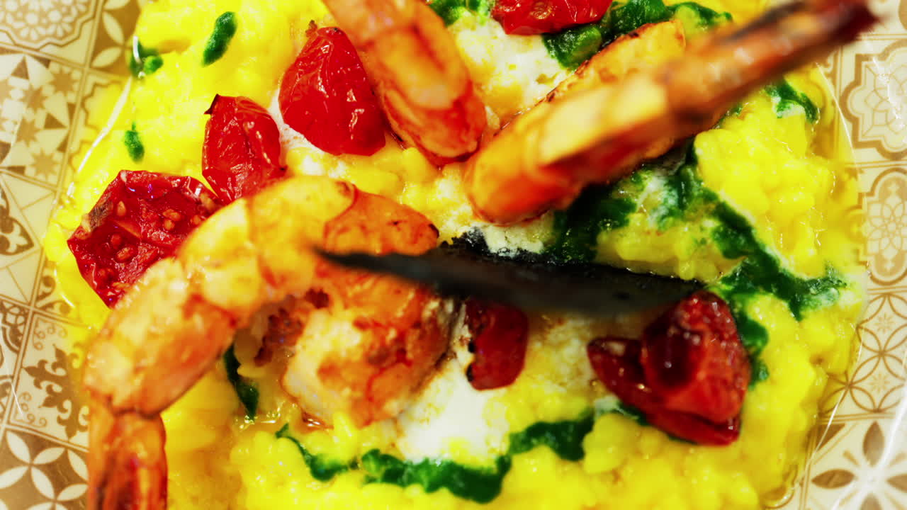 Close up of saffron risotto topped with grilled prawns and roasted cherry tomatoes