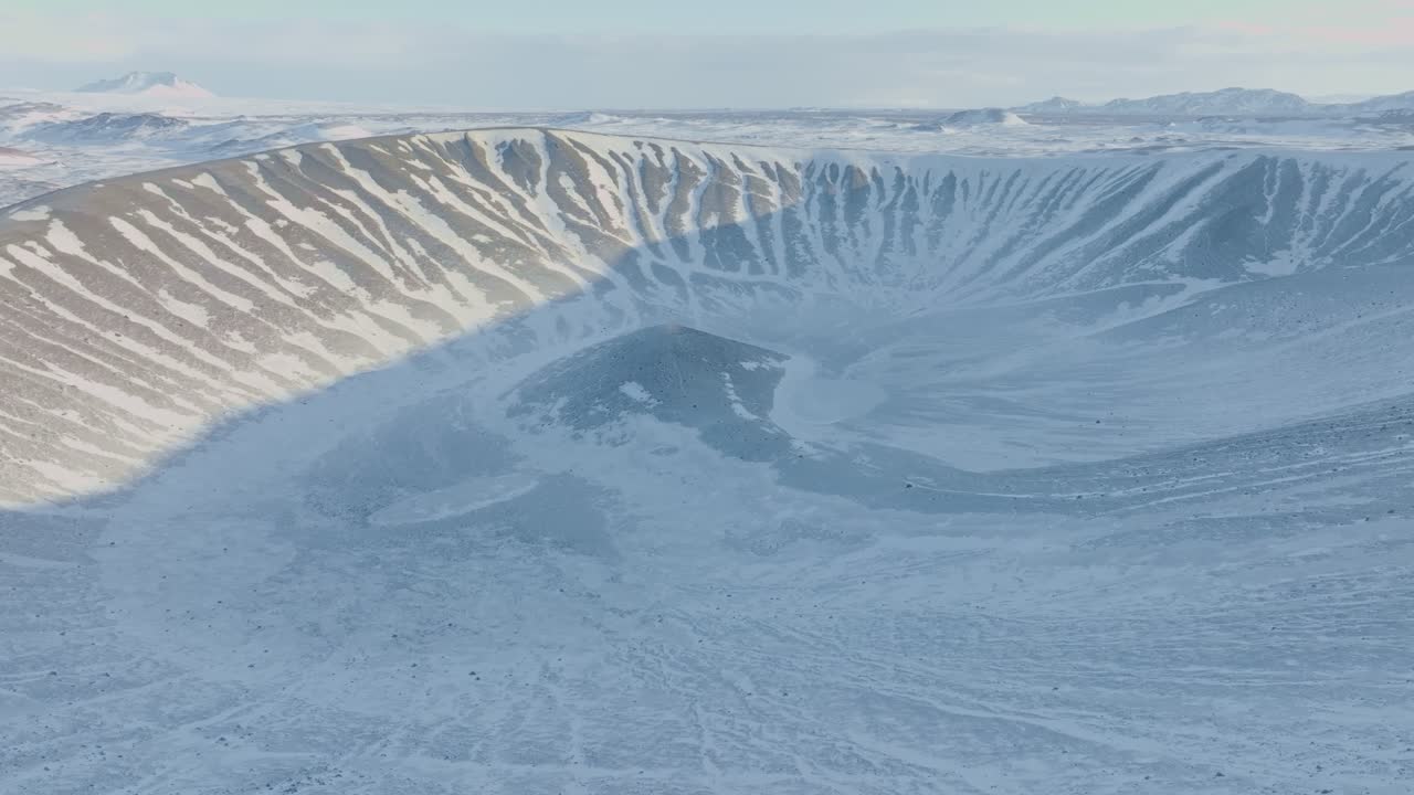 Aerial moving forward drone shot of Hverfjall volcano in Iceland, region of Mývatn, motion towards the crater. In daytime winter, volcano covered with snow. People hiking  on the edges