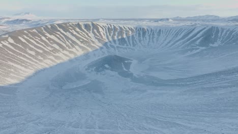 aerial moving forward drone shot of hverfjall volcano in iceland, region of mývatn, motion towards the crater. in daytime winter, volcano covered with snow. people hiking  on the edges