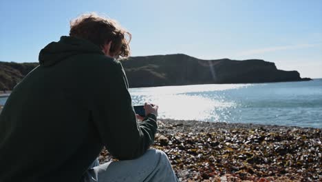 a young watches his phone on lulworth cave beach, morning landscape