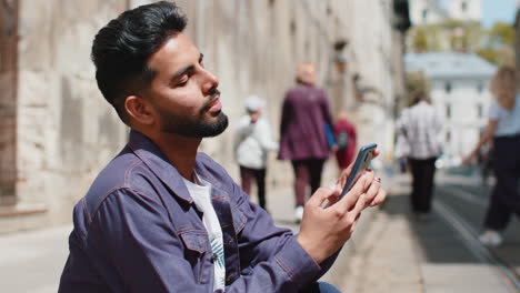 Indian-man-use-smartphone-typing-text-messages-browsing-internet-finishing-work-looking-at-camera