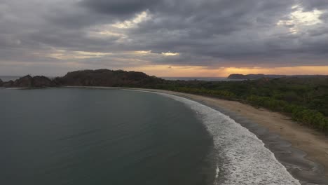 Costa-Curva-De-Media-Luna-De-Costa-Rica-Con-Olas-Suaves-En-La-Orilla-Arenosa-Al-Atardecer,-Tiro-Aéreo