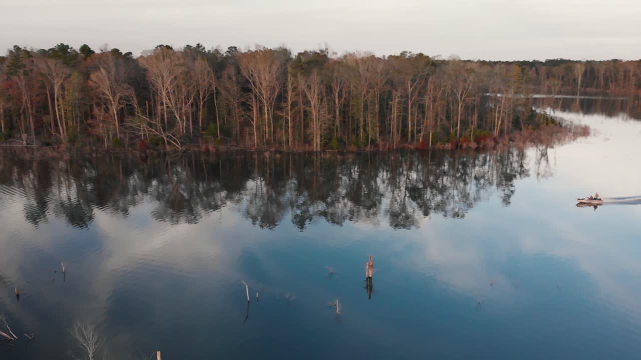 seguir a un solo barco de pesca mientras navega a toda velocidad por la superficie lisa de un lago a la luz dorada del atardecer, y regresar a la rampa para botes cuando se pone el sol