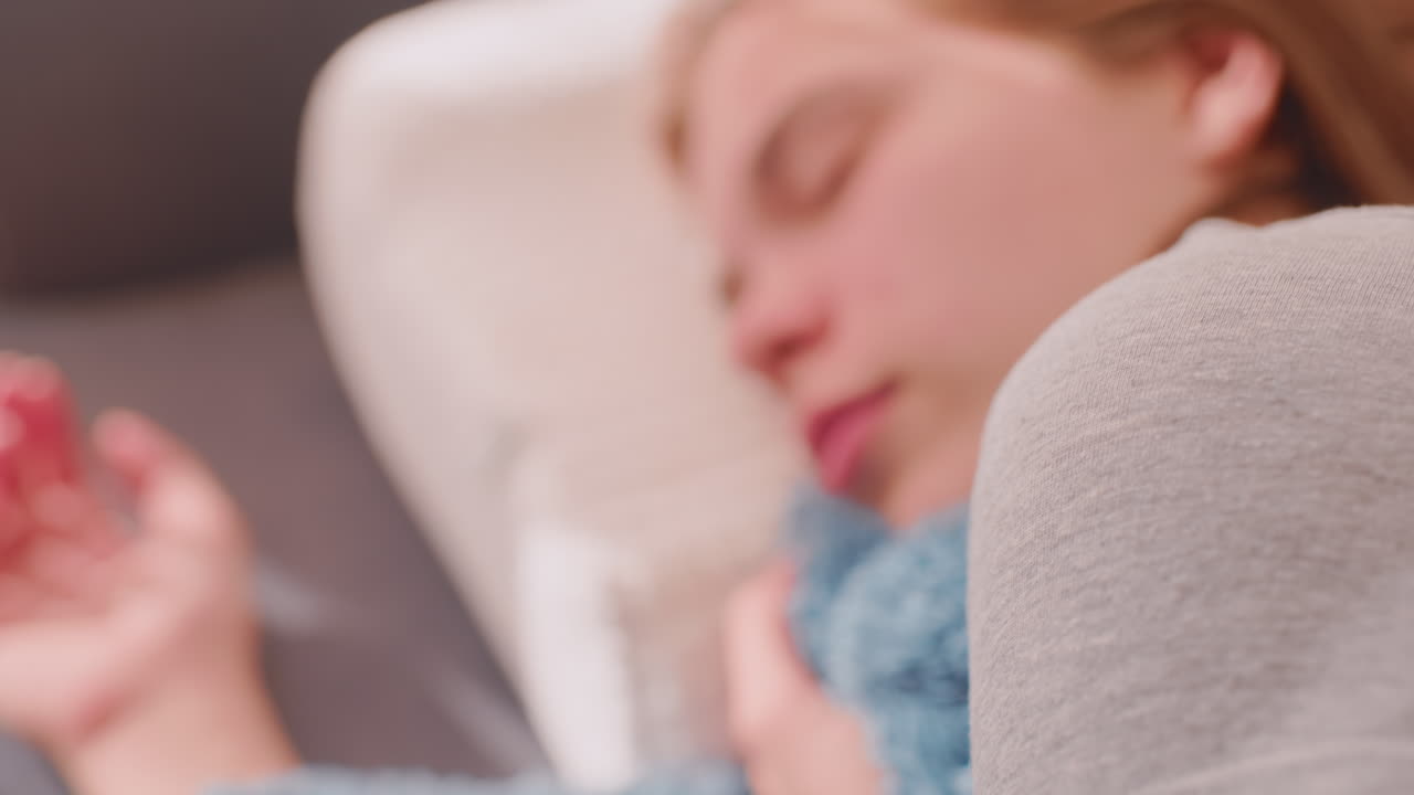 Close up of young woman sleeping peacefully on pillow with blue blanket, hand relaxed, face calm and serene, warm sunlight filling room, dreamy atmosphere showing comfort