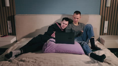 two men watching something on a laptop in bed