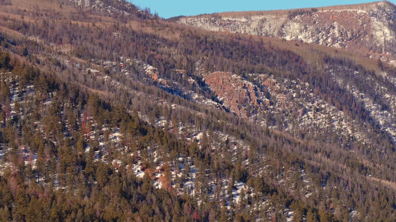 Un elicottero di soccorso dedicato vola seguendo uno schema di ricerca lungo un fianco montuoso impervio. Il filmato sottolinea le condizioni difficili di una missione invernale tra fitta vegetazione e terreno ghiacciato