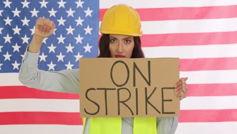 woman in hard hat holding an "on strike" sign in front of an american flag
