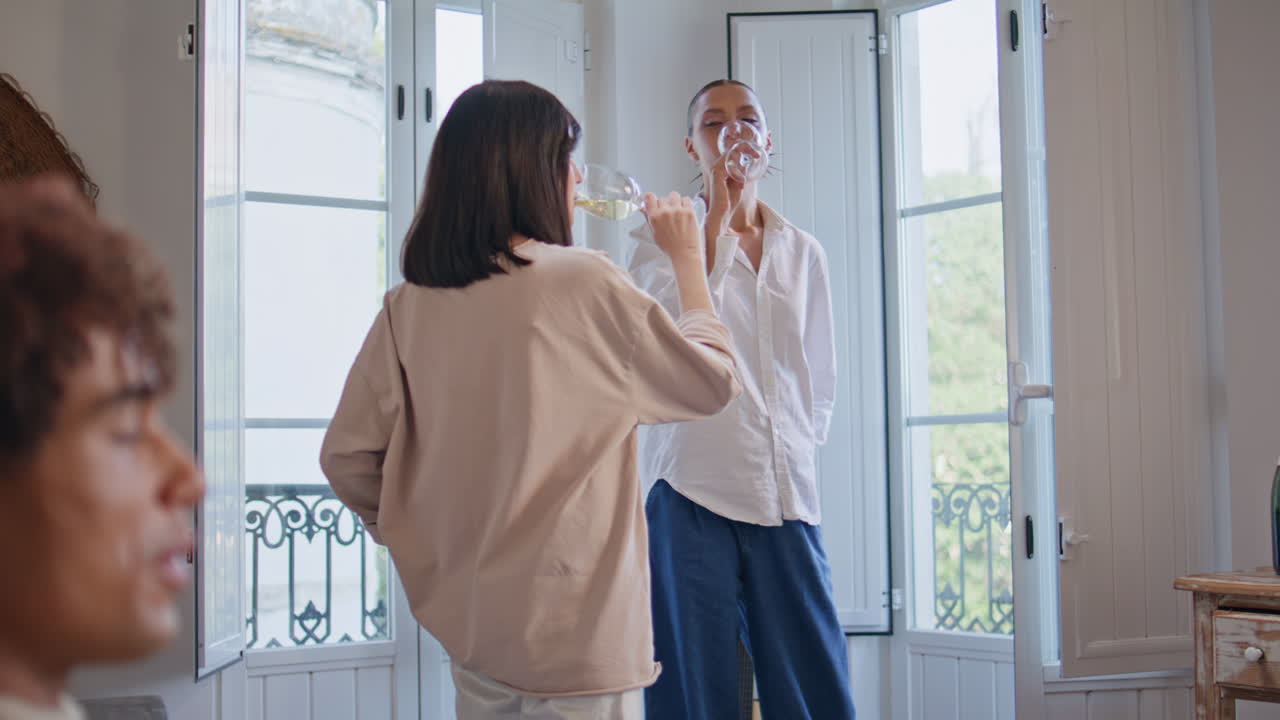 Two girls clinking wineglasses celebrating weekend at home. Friends laughing