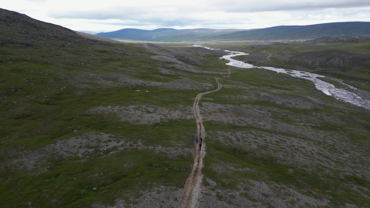 Hikers walk rugged rocky road across expansive northern river tundra