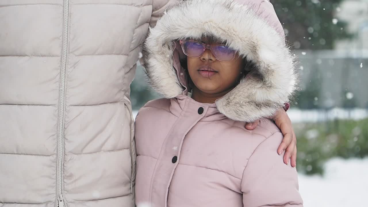 A child in a winter coat stands next to their parent in the snow