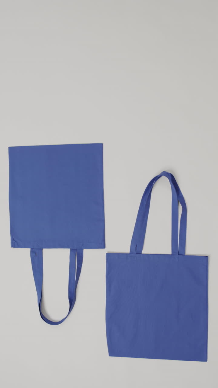 Vertical video of high angle view of two blue canvas bags with copy space on white background