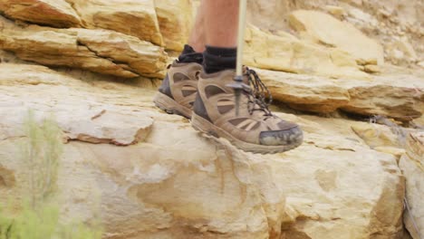 pés de sobreviventes masculinos caminhando por terrenos rochosos em botas de caminhada e usando paus de caminhada