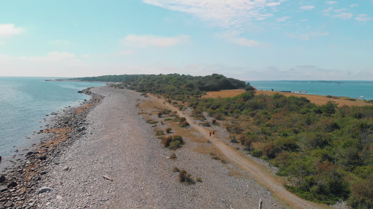 пара бежит трусцой вместе в красивом пейзаже вдоль каменного пляжа у океана летом - аэрофотосъемка 4k