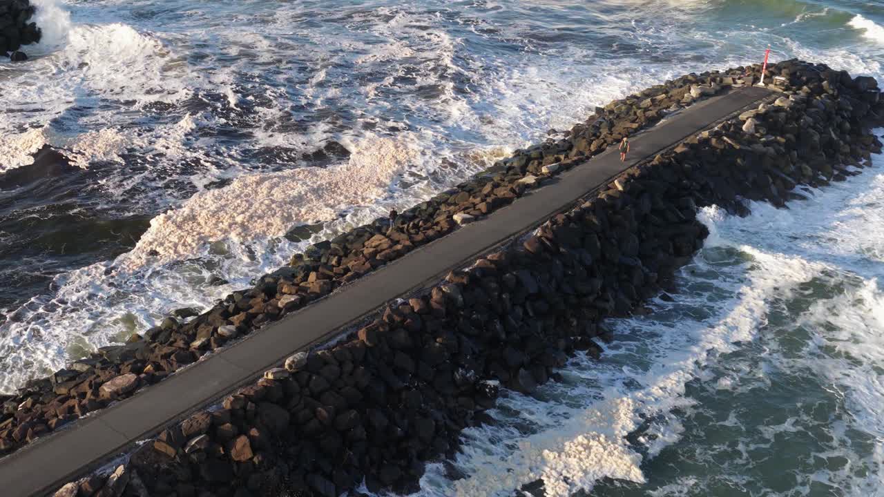 Aerial view of waves crashing against a rocky jetty at Brunswick Heads, NSW. Dynamic ocean scene with strong lighting and movement