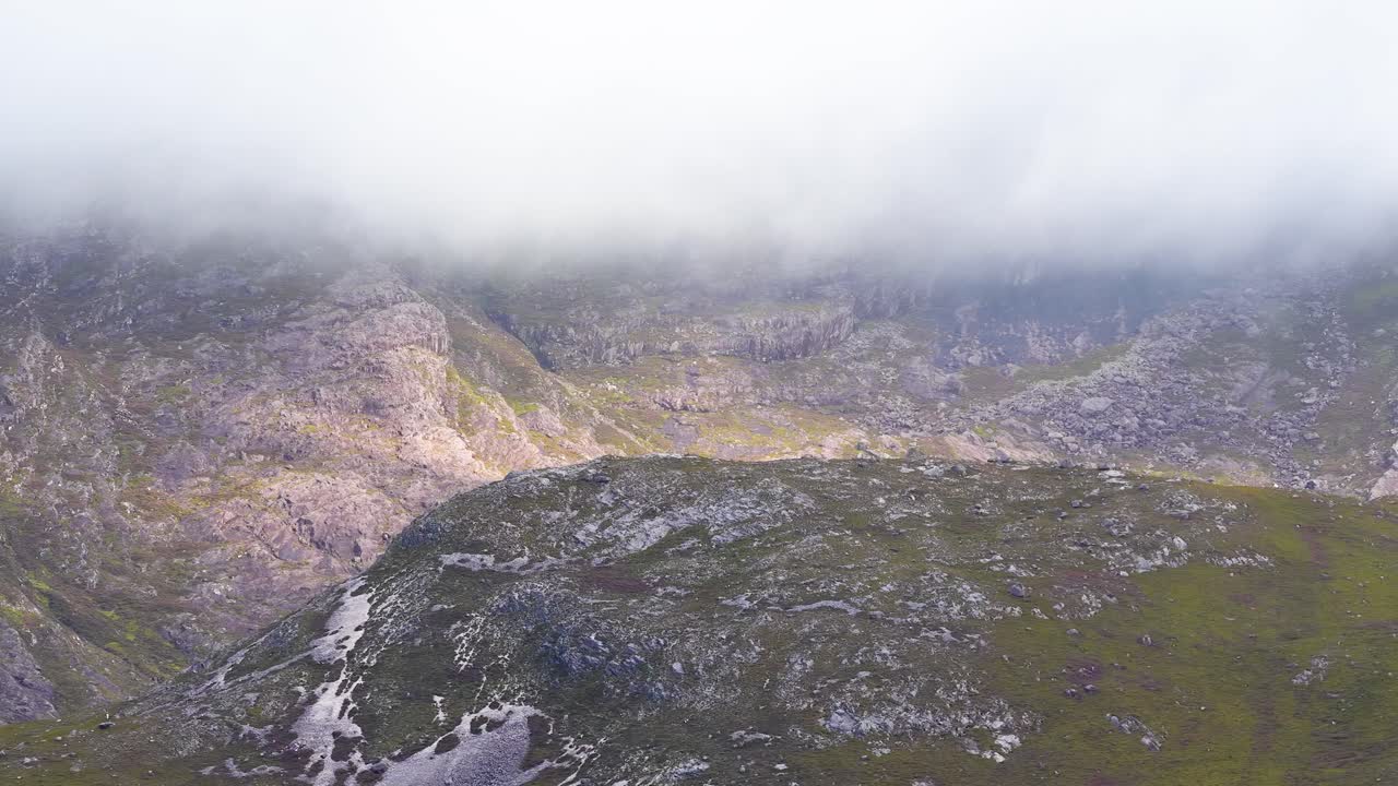 Static wide shot of rocky mountain peak shrouded in mist, soft natural daylight, tranquil mood
