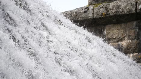 primer plano de la parte superior de una presa de un embalse con agua en cascada sobre la parte superior como una cascada