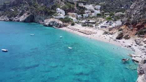 drone reveals behind rock the stunning kira panagia beach in karpathos, greece, with turquoise sea and red church.