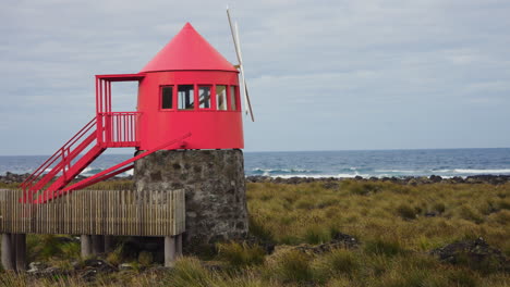 static close up shot of small red windmill located at the rocky coastline