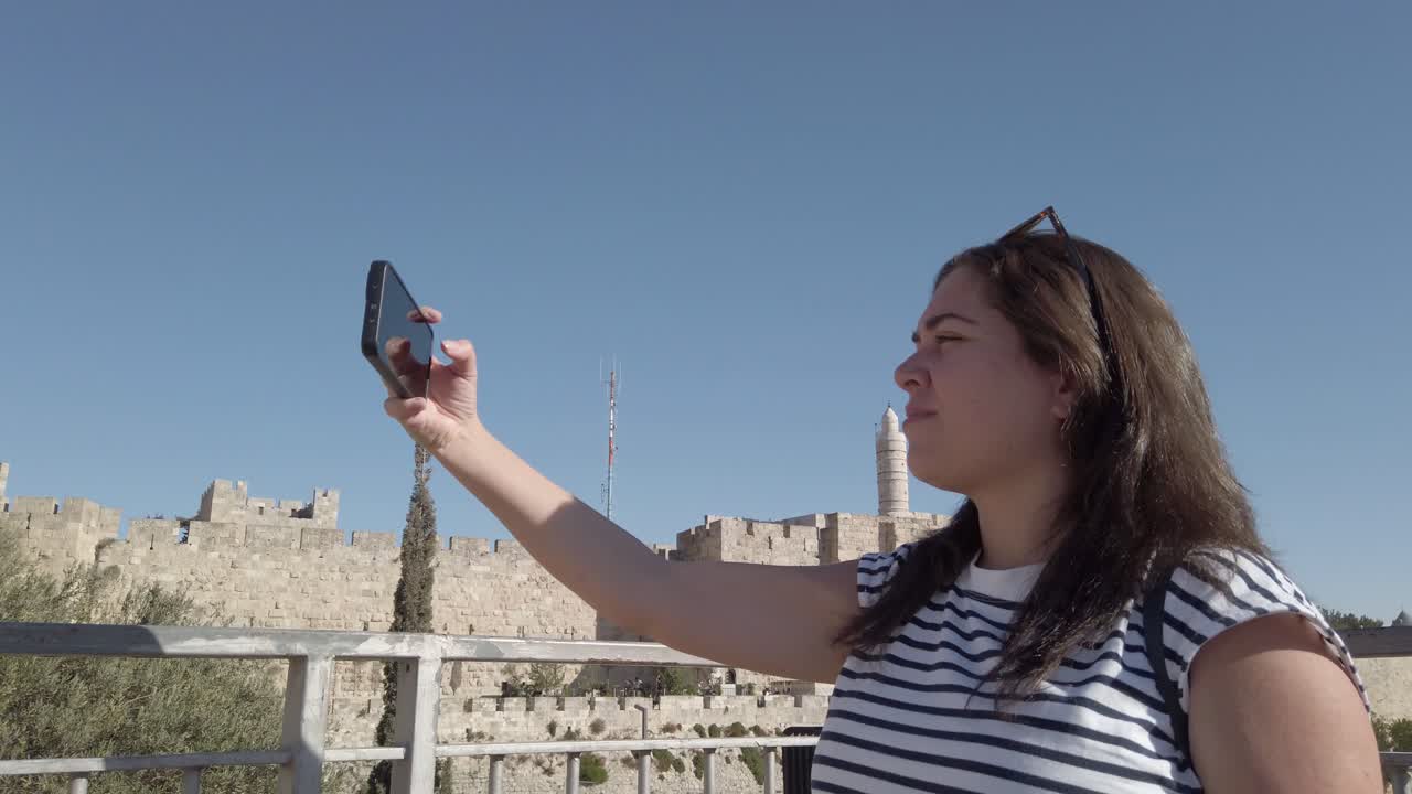 mujer tomando una selfie frente a una antigua muralla de la ciudad