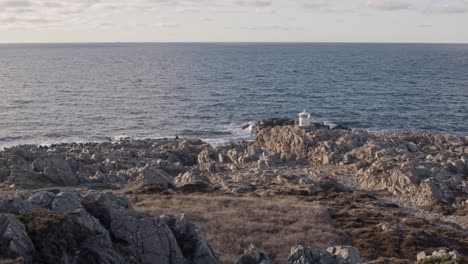 Small-lighthouse-at-the-cape-of-rocky-cliff-at-sunset-and-golden-hour