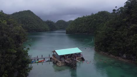 Aerial,-Tourists-swimming-by-floating-pontoon-style-lodge-of-Sugba-Lagoon-in-Siargao-Island,-Philippines