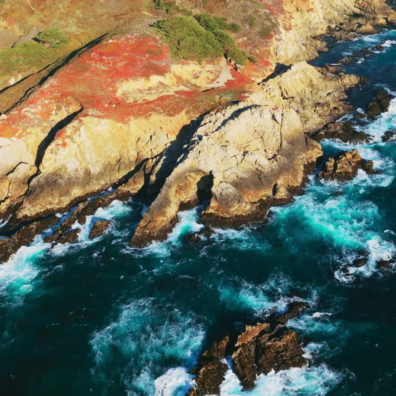 Pacific ocean meeting the rocky shore of California. Foamy white waves crushing at rugged bare mountains on sunny day. Top view
