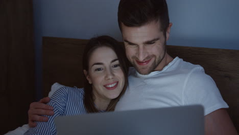 Sonriente-Pareja-Joven-Caucásica-De-Buen-Aspecto-Viendo-Algo-Divertido-En-La-Computadora-Portátil-En-La-Cama-Por-La-Noche