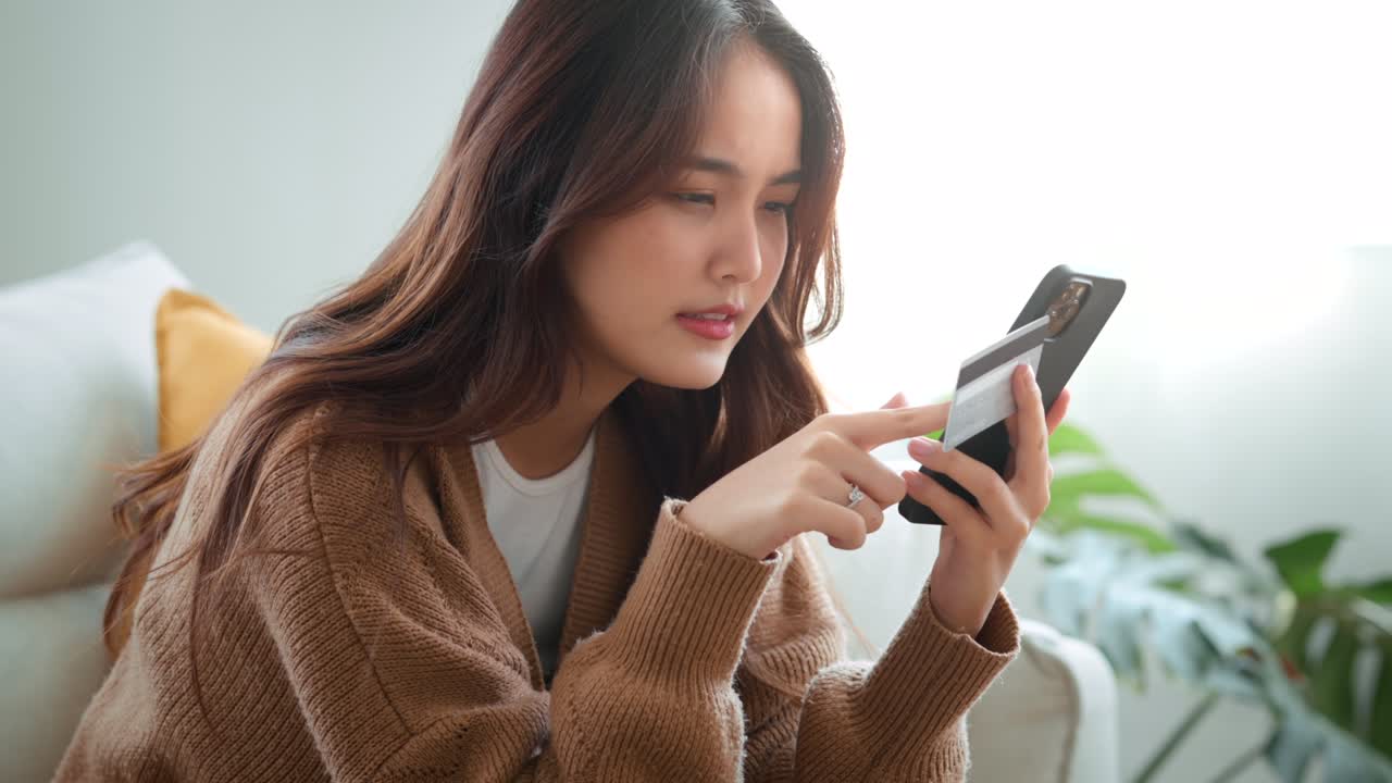 행복한 젊은 아시아 여성은 집에서 즉각적인 모바일 결제를 사용하여 신용카드를 들고 있습니다. 웃는 여성 고객 쇼퍼는 스마트폰에서 구매를 하고 현금 환불 개념을 받습니다.