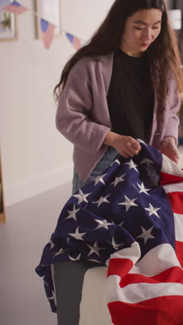 vertical video of woman at home putting american stars and stripes flag on sofa for party celebrating 4th july independence day