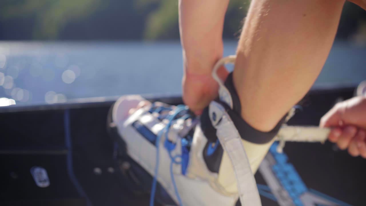 Putting on a wakeboard before a riding session on a lake on a sunny day, strapping board boots