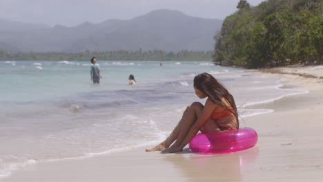 chica latina disfruta jugando con arena y agua sentada en la playa de una isla tropical en un anillo inflable