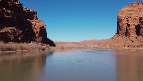 A-tracking-drone-shot-of-a-truck-driving-between-the-steep-cliffs,-known-as-the-“Wall-Street-Climbing-area”,-and-the-Colorado-River,-near-Moab,-Utah