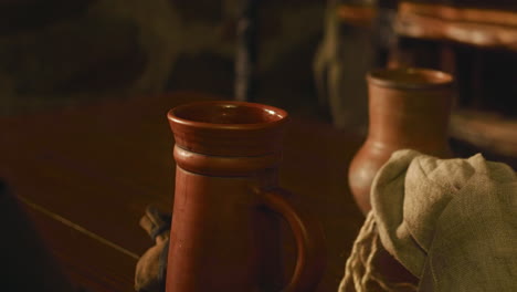 medieval servant puts beer mug on wooden counter closeup. barkeeper serves alcohol drinks in clay dishware in tavern. drinking wine in old fashioned pub