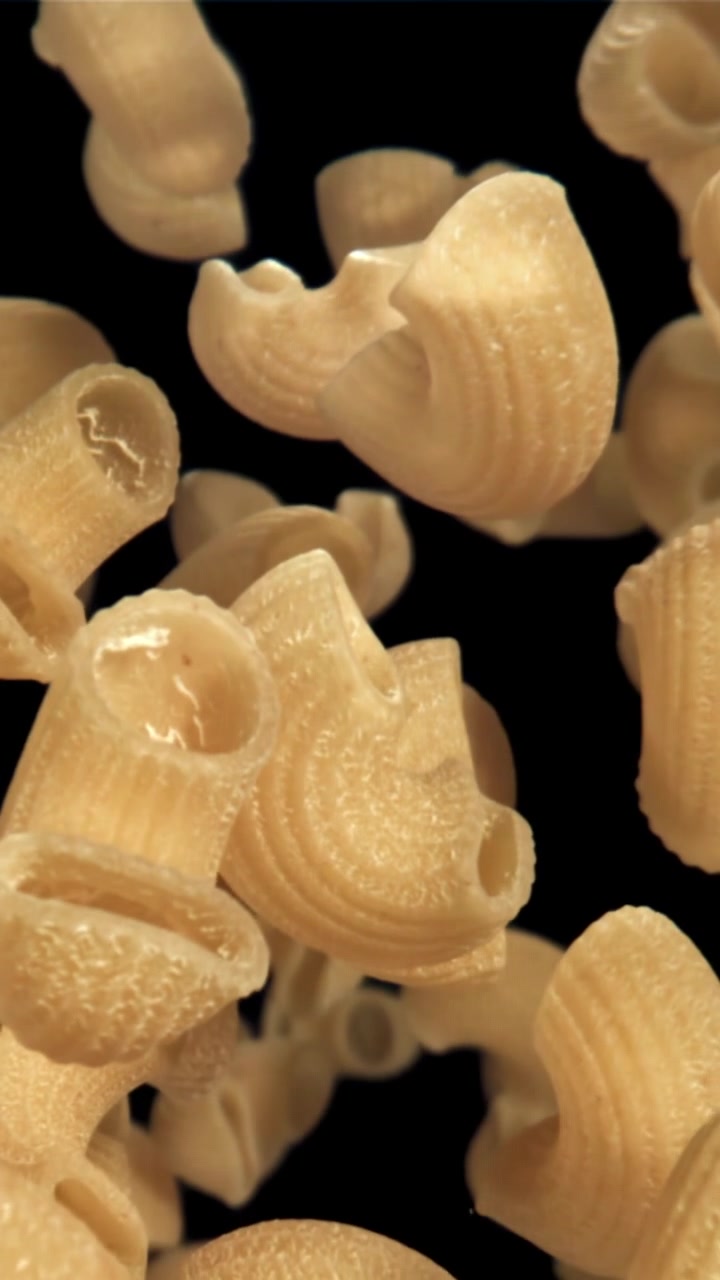 Pasta maccheroni secca che cade al rallentatore su sfondo nero.