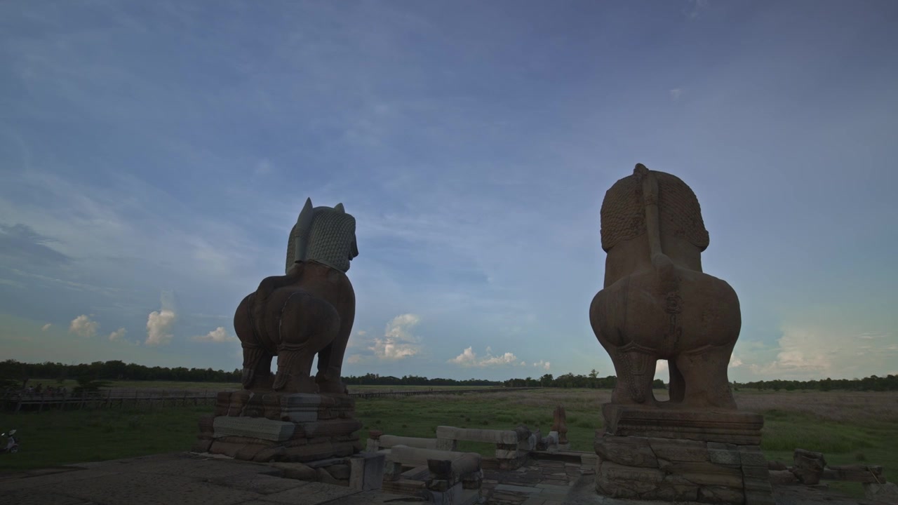 Antik Angkor kumtaşı aslan heykelleri, yağmur mevsiminin başlangıcında otlarla dolu baray gölüne bakıyor. Hareket kontrollü dinamik hareket hızlandırılmış çekim