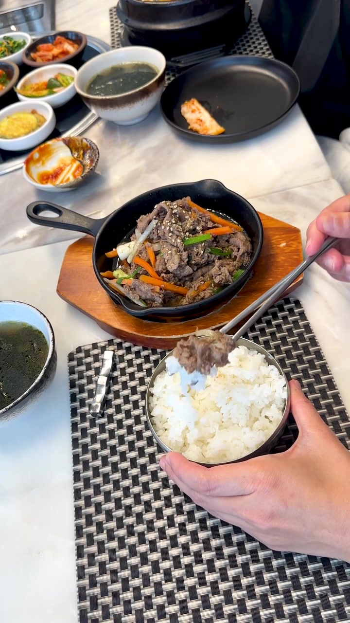 箸を使って白いご飯の丼に牛肉のプルコギを置いている人の真上からのショット。