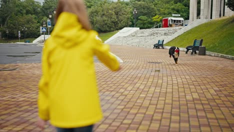 un perro negro feliz corre y lleva una pelota a su dueño una adolescente en una chaqueta amarilla mientras camina y juega en el parque después de la lluvia