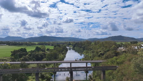 el vuelo se eleva por encima y por encima de los puentes ferroviarios y de carretera en el río pioneer por mirani en la región de mackay de australia.