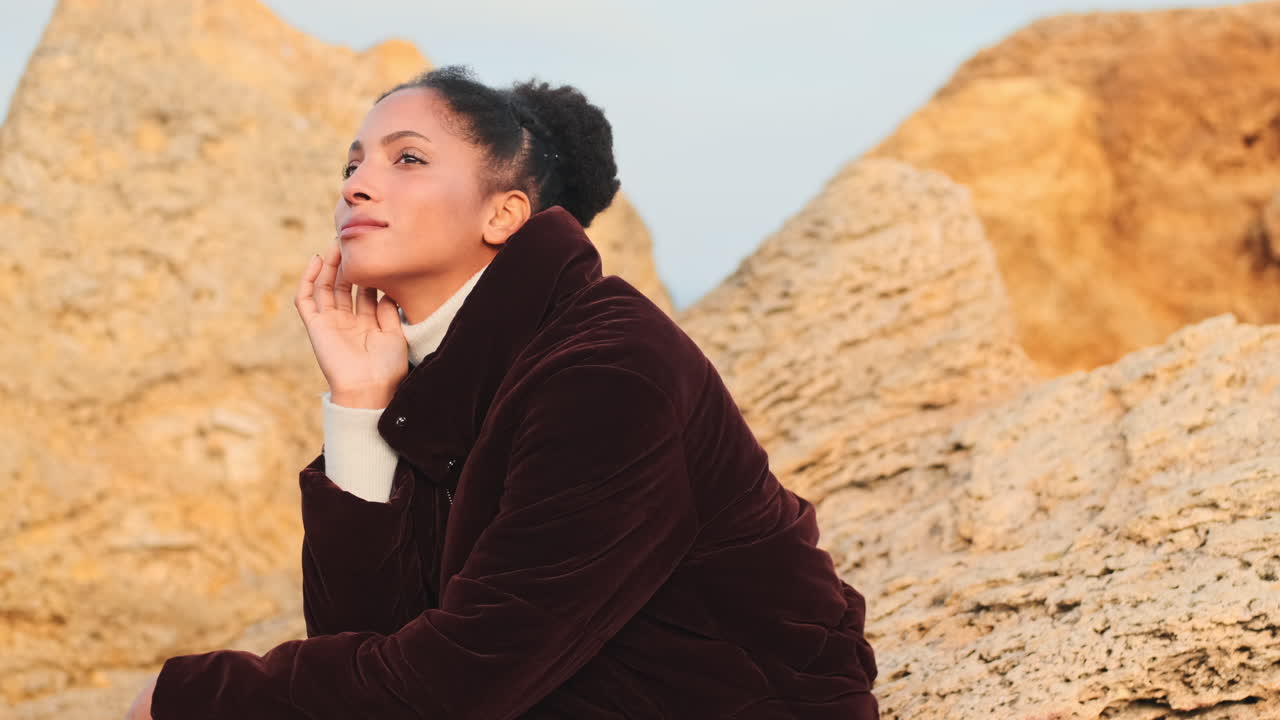 African American girl posing on stones by the sea.