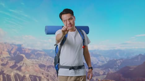 asian male hiker with mountaineering backpack showing no gesture with index finger while traveling at the top of mountain
