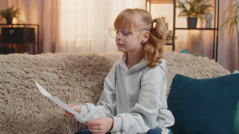 young teenager girl wearing glasses at home sofa studying documents and receipts serious expression