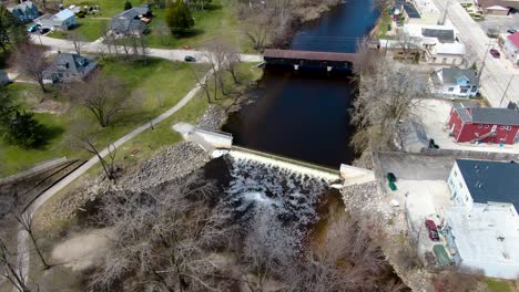 aerial fly-over the historic covered wooden bridge over the creek in a small american town - establishing shot