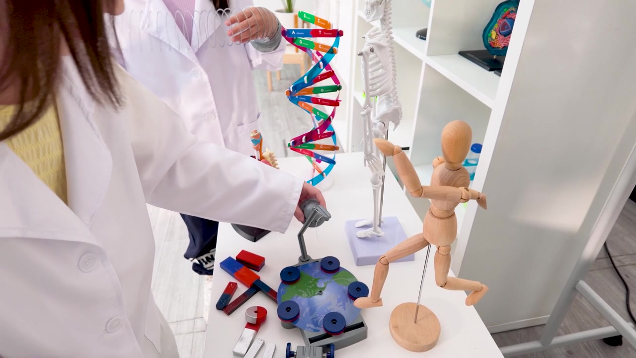 Jovens estudantes em jalecos brancos examinam modelos de DNA e anatomia durante uma aula de ciências.